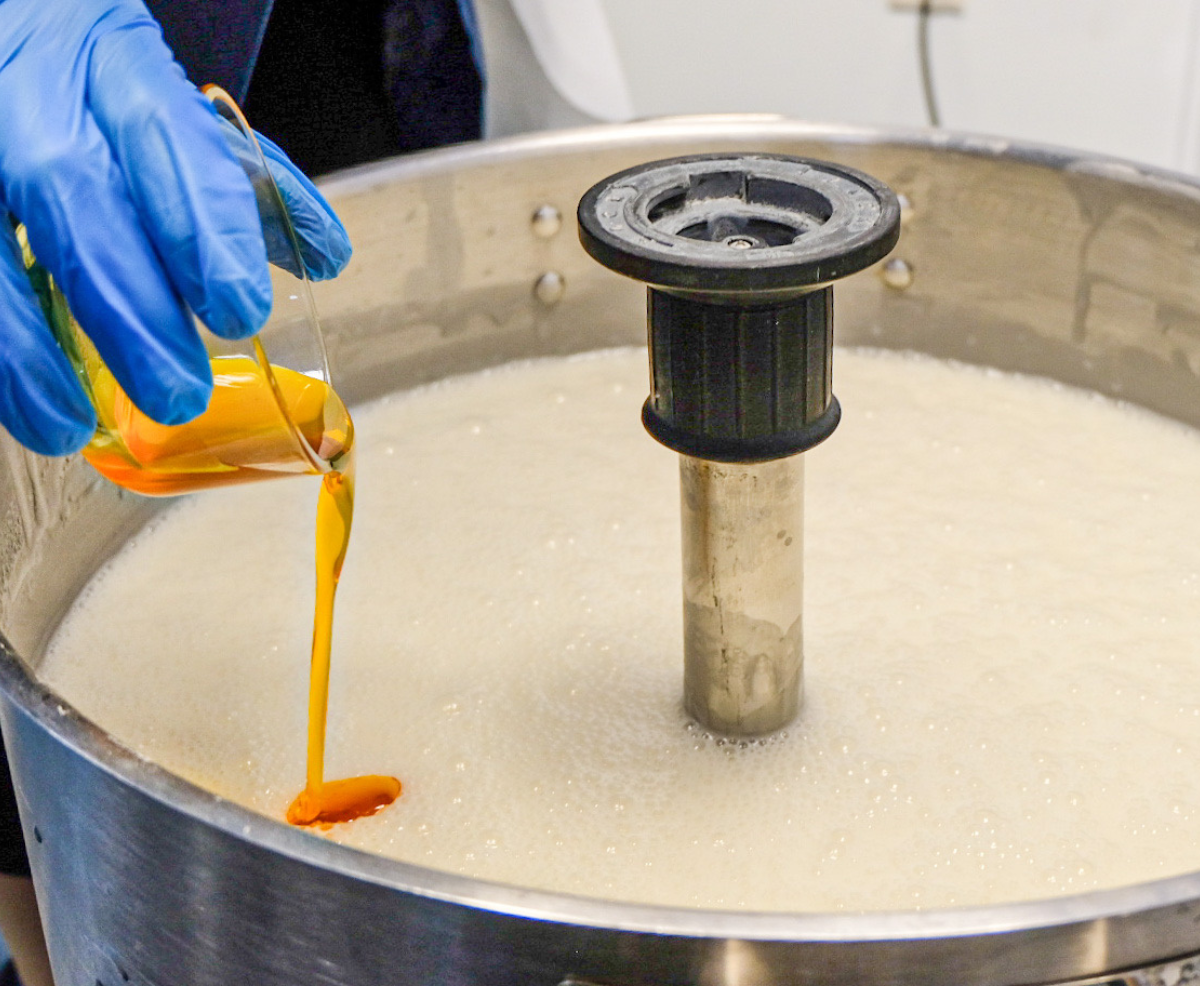 A product-formulator pouring an ingredient into a mixing vessel