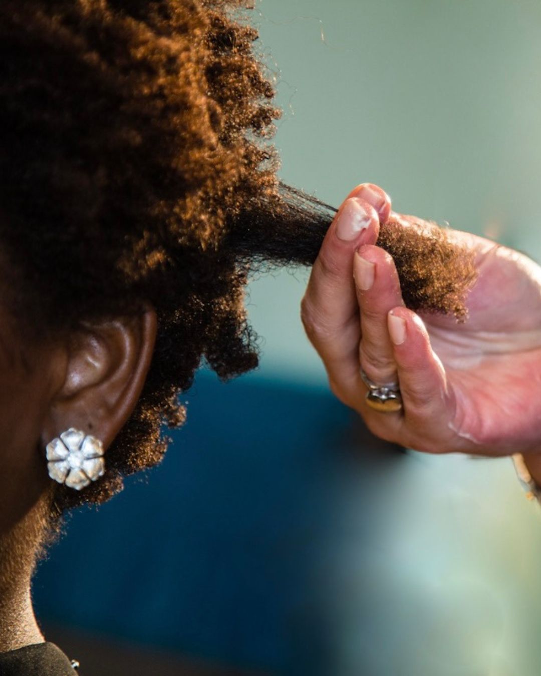 A close up shot of a woman with an earring, her curly hair being examined in a stylists hand